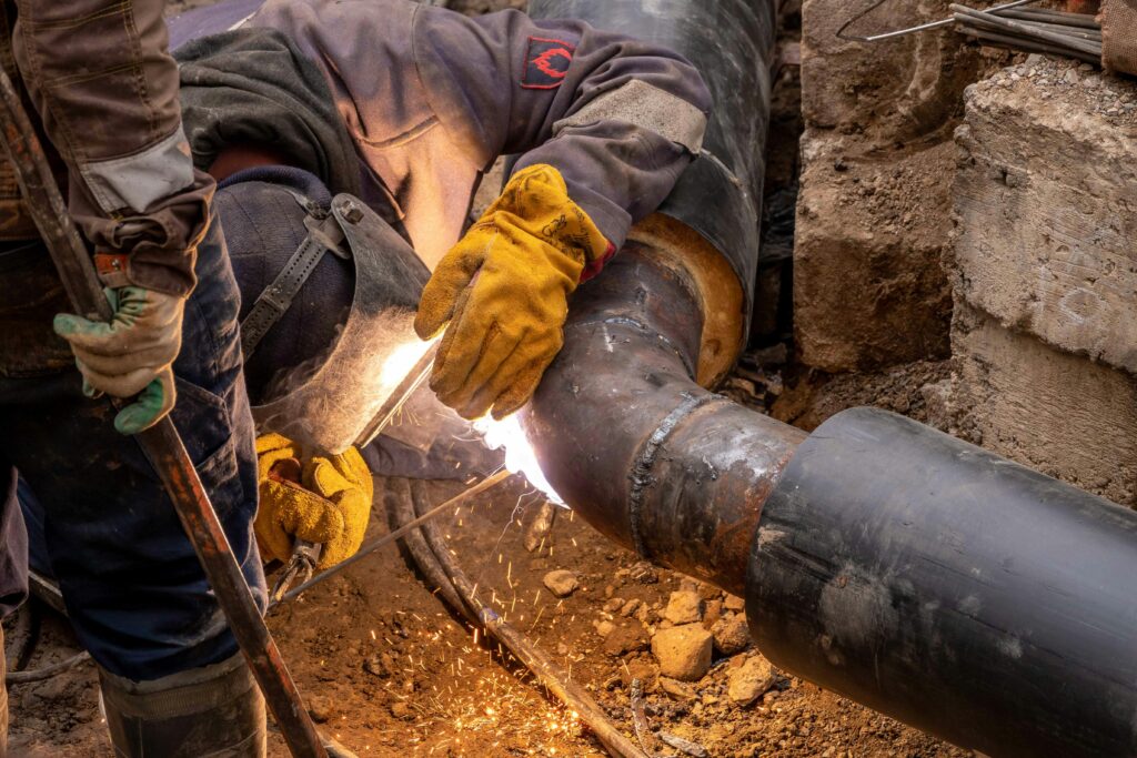 Close-up of a skilled worker welding steel pipes in an industrial setting, showcasing expertise and safety gear.